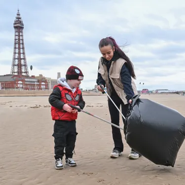 An adult and child litter picking on Blackpool Beach in front of The Blackpool Tower