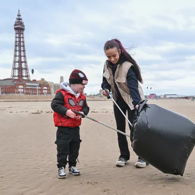An adult and child litter picking on Blackpool Beach in front of The Blackpool Tower