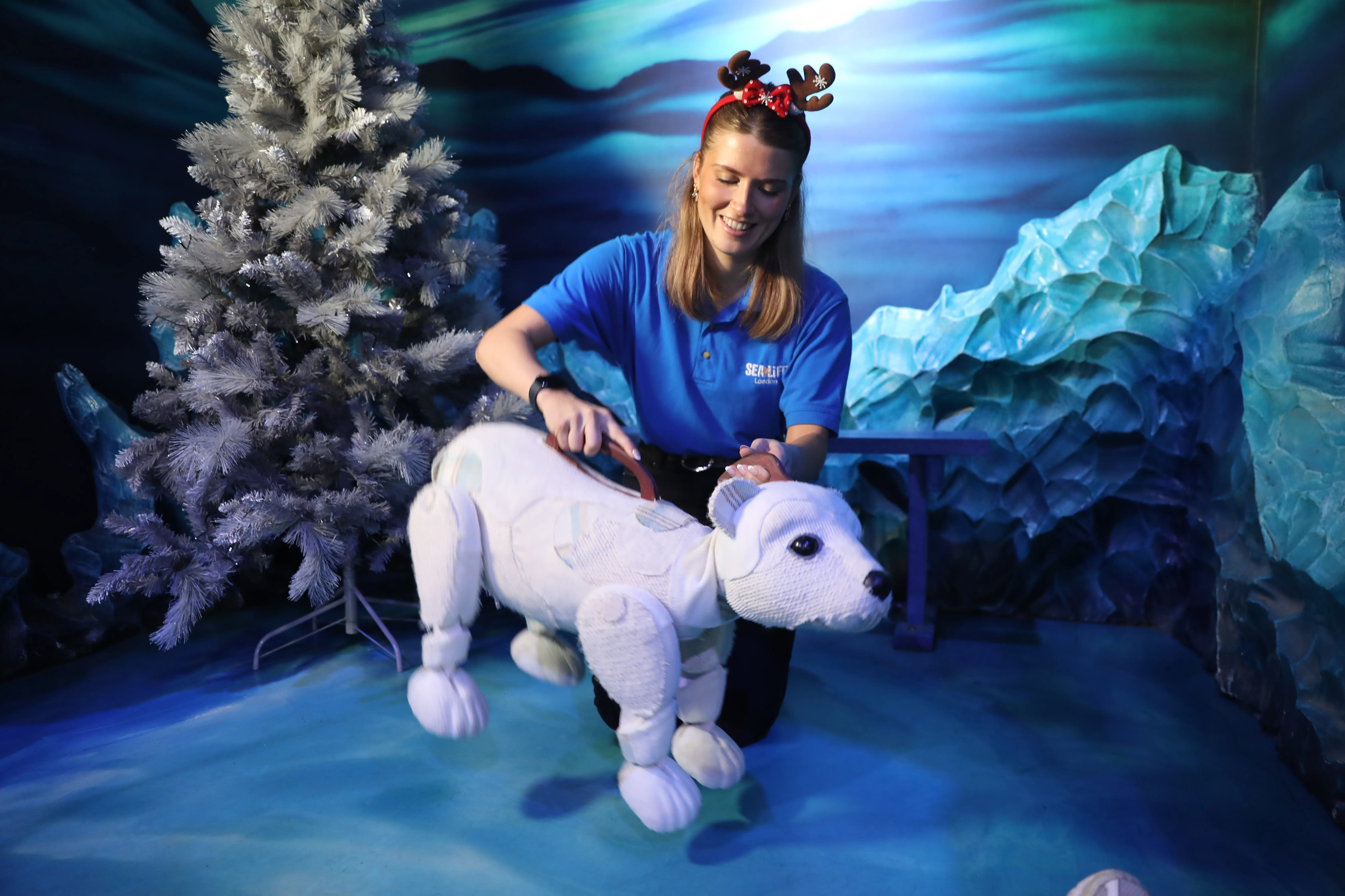 SEA LIFE London staff member with Al the Polar Bear Puppet galloping besides a Christmas tree 