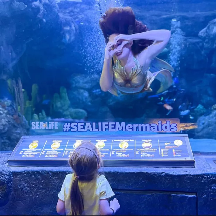 Mermaid making a heart with her hands underwater for a child at SEA LIFE Orlando.